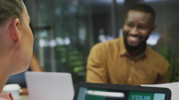 Diverse male and female business colleagues smiling and using laptop