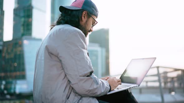 A Young Man in Glasses Working on a Laptop Outdoors