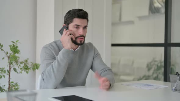 Angry Young Man Talking on Smartphone in Office