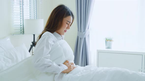 Asian beautiful sick girl in pajamas getting up having stomach ache or periods on bed in bedroom.