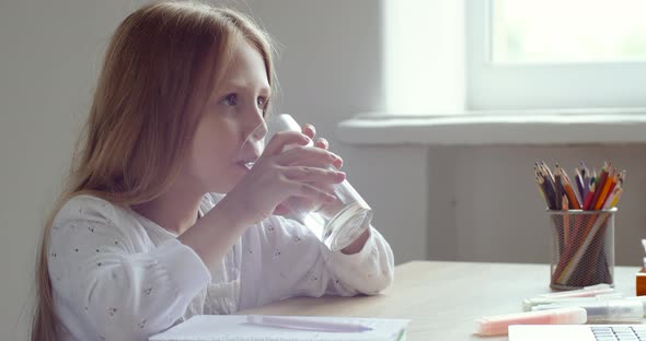 Schoolgirl Sits at Home Table Takes Break During Homework, Feels Thirsty Picks Up Transparent Glass