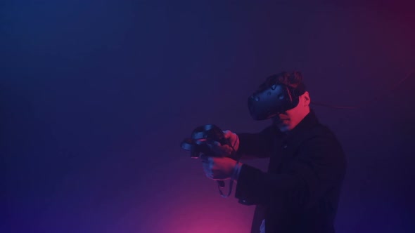 Young Man Gamer in Virtual Reality Headset Playing Online Shooting Game, Using Controllers To Shoot