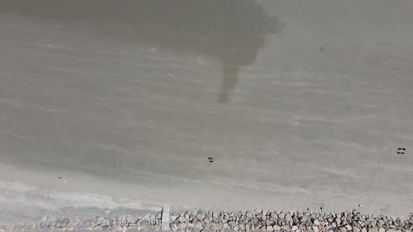 Aerial Top down drone view of a beach at low tide. Walkers and birds are visible. Beach. Sea wall.