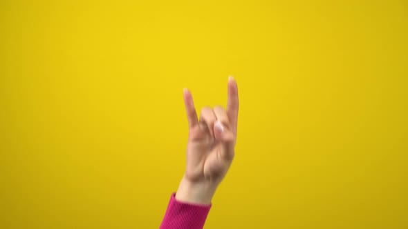 Female Hand Shows the Sign of the Horns. Studio Photography on an Isolated Yellow Background