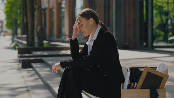 Sad Woman Sitting with Wooden Box of Office Items Outdoors