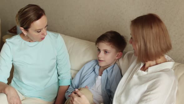 Two Adult Women and a Child are Sitting on the Couch Chatting and Smiling