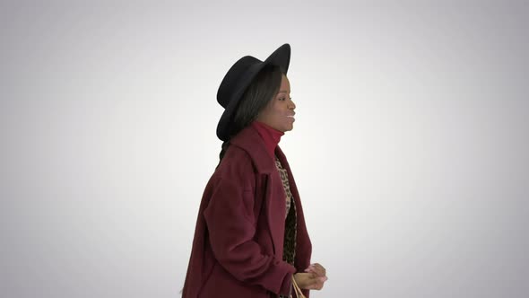 Smiling African American Fashion Girl in Coat and Black Hat Posing with Shopping Bags on Gradient