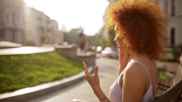 Emotional Redhead Girl Talking on Phone Sitting on Bench Outdoors Slow Motion