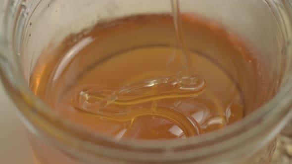 Clear golden runny honey dripping into a jar close up