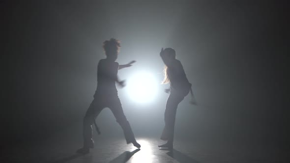 Strong Ladies Practicing Capoeira in Darkness Against Spotlight in Studio