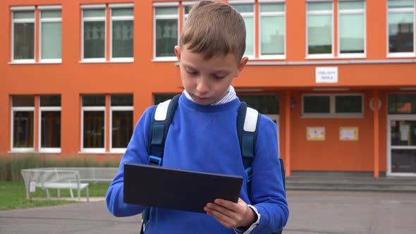 A Young Boy Works on a Tablet in Front of an Elementary School