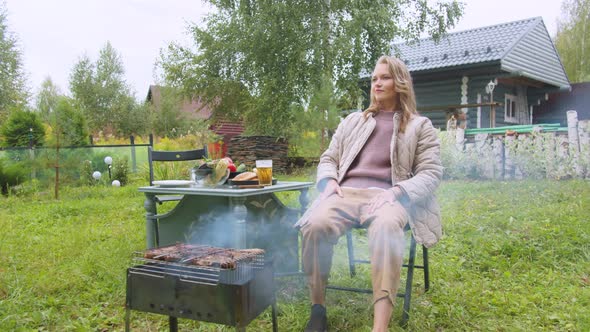 Lonely Sad Woman Is Bored in the Yard of a Country House, She Makes a Barbecue and Drinks Beer in