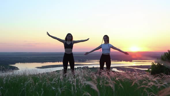 Two Young Women Standing on a Green Field and Doing Warming Up Exercises