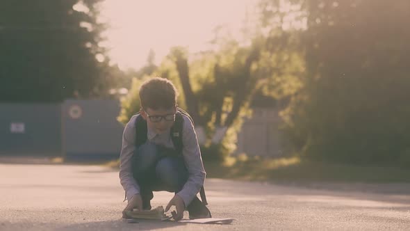 Boy in Shirt and Jeans Gathers Books and Sheets on Asphalt