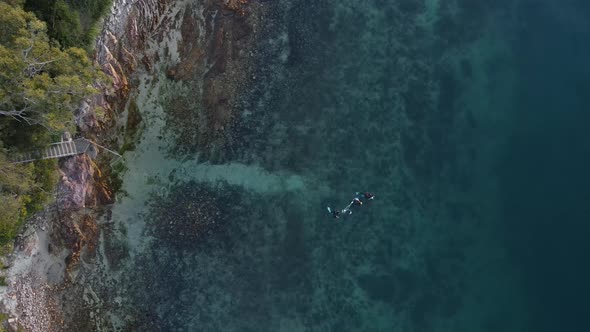 High view of a group of scuba divers swimming out to a sunken tropical reef in blue water. Drone vie