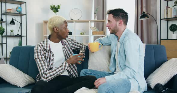 Mixed Race Gay Couple which Drinking Tea at Home During Pleasant Joint Conversation