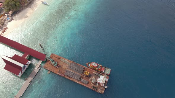 Industrial ferry boat with pipes delivery unloaded at dock of luxury Gili Island during Covid19.