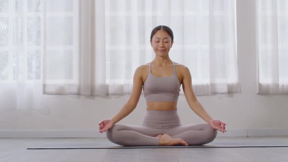 Calm of Attractive Asian woman and grey sport ware practice yoga lotus pose to meditation at home