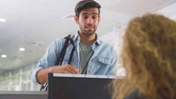 Caucasian male passenger handing phone to airline staff for scanning at check in counter in airport