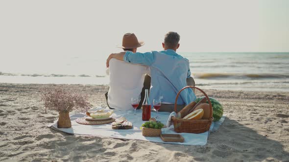 Homosexual Lgbt Couple Gay Men Having Picnic at Beach Sitting on Blanket and Embracing Looking to
