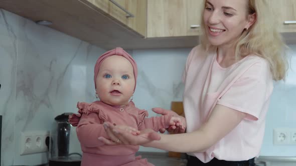 The Mother Plays with the Baby Holding Her Hands While the Baby is Full on the Kitchen Counter