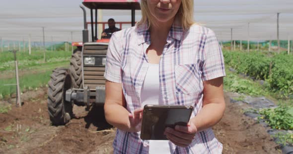 Video of happy caucasian woman standing with tablet in front of tractor