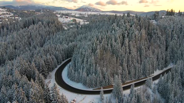 Aerial view of winter landscape with snow covered mountain hills and winding forest road in morning.