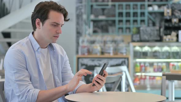 Young Man Loss on Smartphone in Cafe