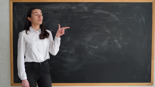 Caucasian Student Girl Stands Near the Chalk Board Raises Her Index Finger and Points to an Empty