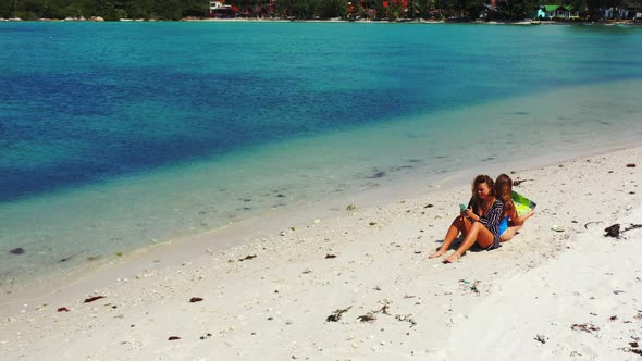 Beautiful smiling ladies on photoshoot in the sun at the beach on clean white sand and blue 