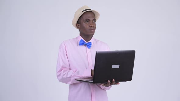 Young Happy African Tourist Man Thinking While Using Laptop