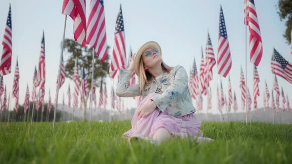 Slow Motion Woman Sitting on Green Grass and Looking on Many American Flags
