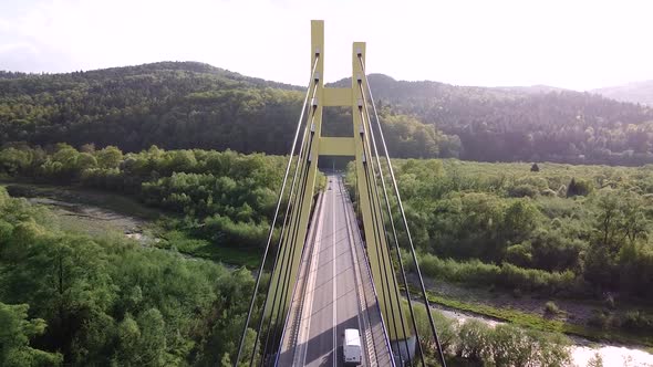 flying through huge yellow bridge, moving cars, trees, forest - drone shot