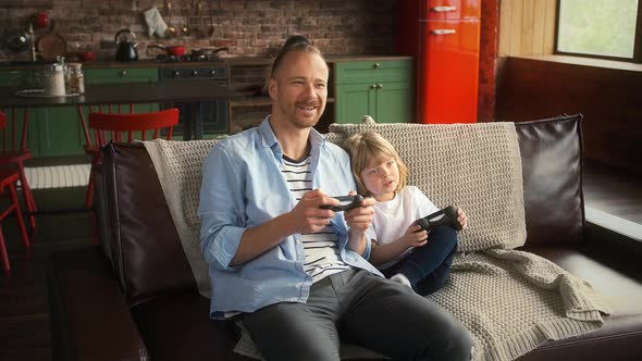 Father and His Son are Smiling Holding Wireless Joysticks and Playing Video Game on Console While