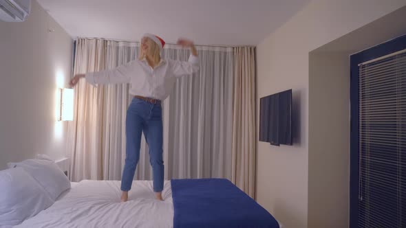 slender beautiful girl dancing in a Santa Claus hat on the bed.