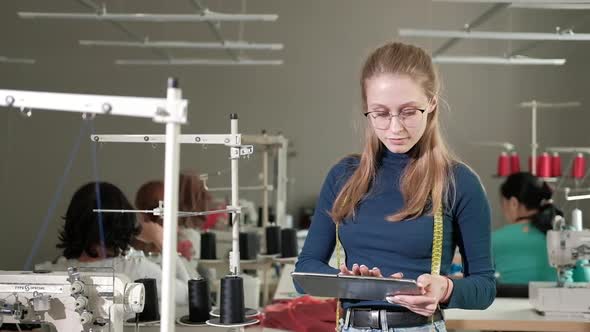 successful dressmaker stands in a sewing shop and works with tablets in hands