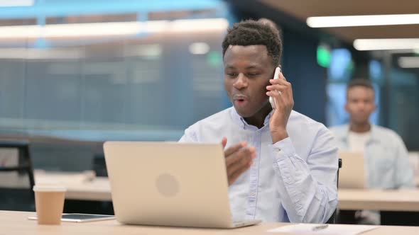 Angry African Businessman with Laptop Talking on Smartphone