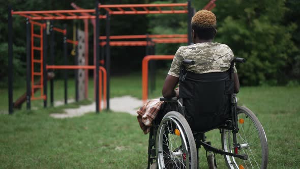 Back View Sad Young African American Military Man in Wheelchair on the Right Looking at Sports