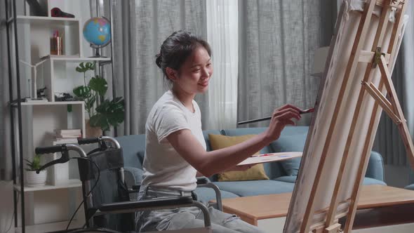 Asian Artist Girl In Wheelchair Holding Paintbrush Mixed Colour And Painting On The Canvas