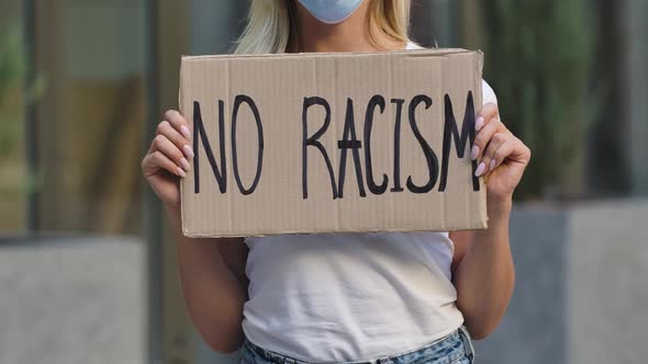 NO RACISM on a Cardboard Poster in the Hands of Female Protester Activist. Closeup of Poster and