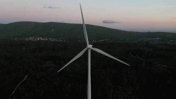 Wind Turbines Spinning Slowly On Dense Foliage Forest With Tranquil Village At The Background In Ser