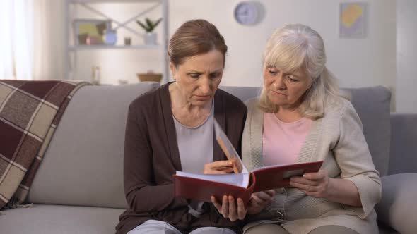 Upset Women Looking Through Photo Album Remembering Past Times, Sad Memories