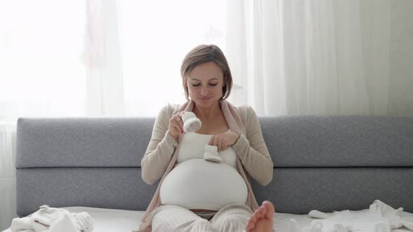 Young Pregnant Woman with Small Baby Shoes Sitting on Sofa at Home