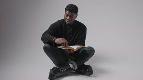 Young Bearded AfroAmerican Man Reads a Book in Studio Over Grey Background Full Shot Isolated Copy