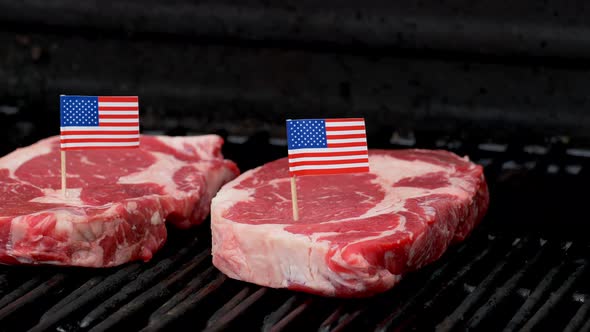 Two juicy rib-eye steaks sitting on the grill and cooking with two tiny American flags tooth picked