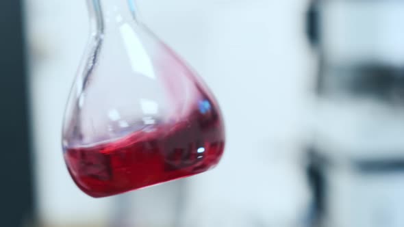 Laboratory Flask with Liquid Shaken on Blurred Background