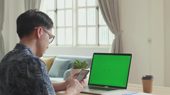 Asian Man Use Smart Phone And Laptop Computer With Green Screen Display At Home