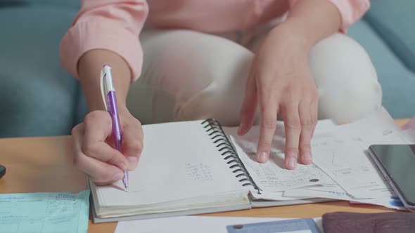 Close Up Of Woman's Hand Holding The Bill And Recording The Expenses In Notebook