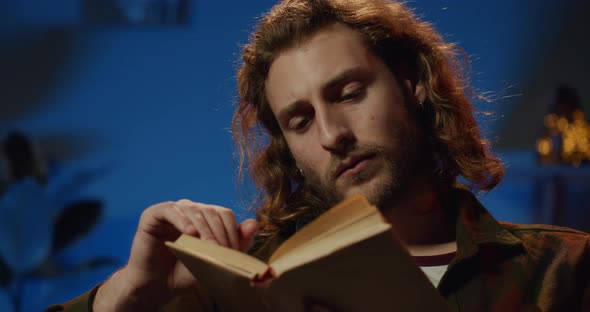 Millennial Handsome Guy Reading Interesting Literature and Turning Page While Looking tired
