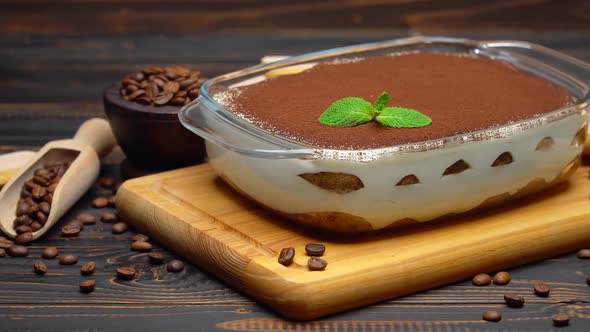 Italian Tiramisu Dessert in Glass Baking Dish on Cutting Serving Board on Wooden Background